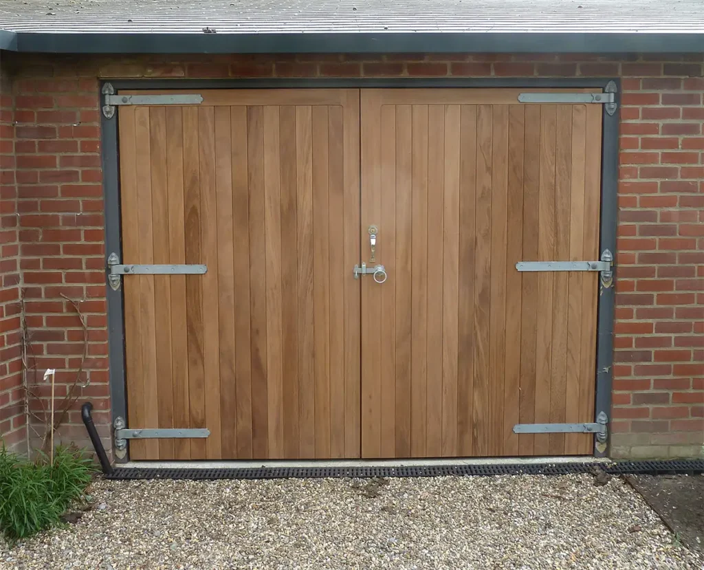 Bespoke timber side-hinged garage door on a residential property with a natural wood finish and traditional ironwork hinges