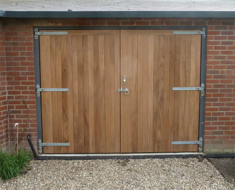 Bespoke timber side-hinged garage door on a residential property with a natural wood finish and traditional ironwork hinges