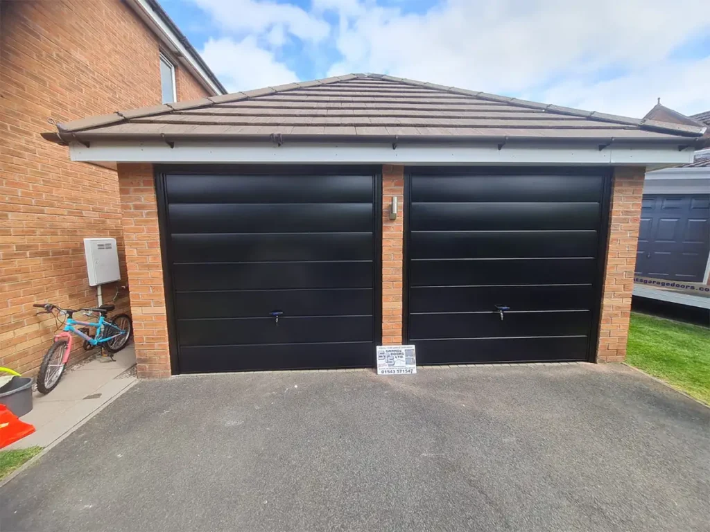 Black steel twin up-and-over garage door on a residential property with a sleek modern finish and classic panelled design