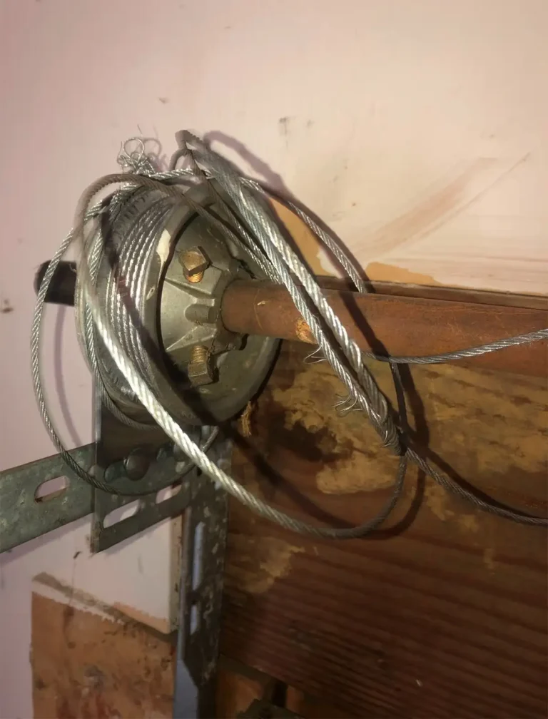 Broken garage door cable that needs replacing, showing a snapped or frayed cable hanging loose from the drum