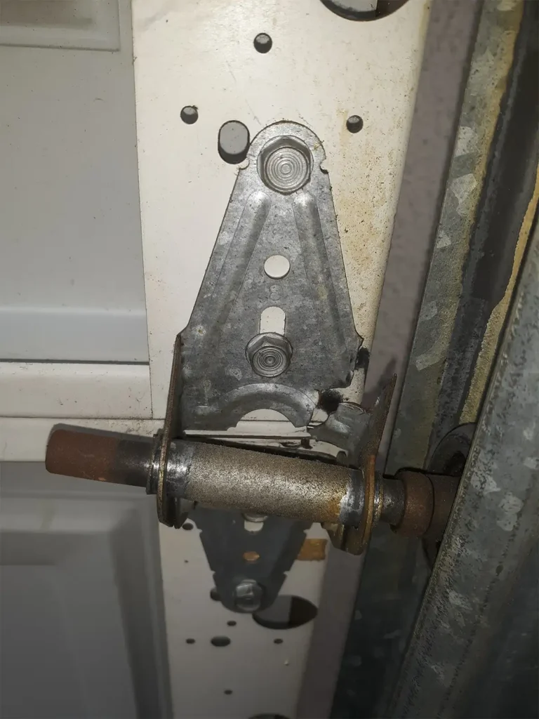Broken garage door roller on track showing a damaged wheel that has come off the guide rail, causing the door to become misaligned