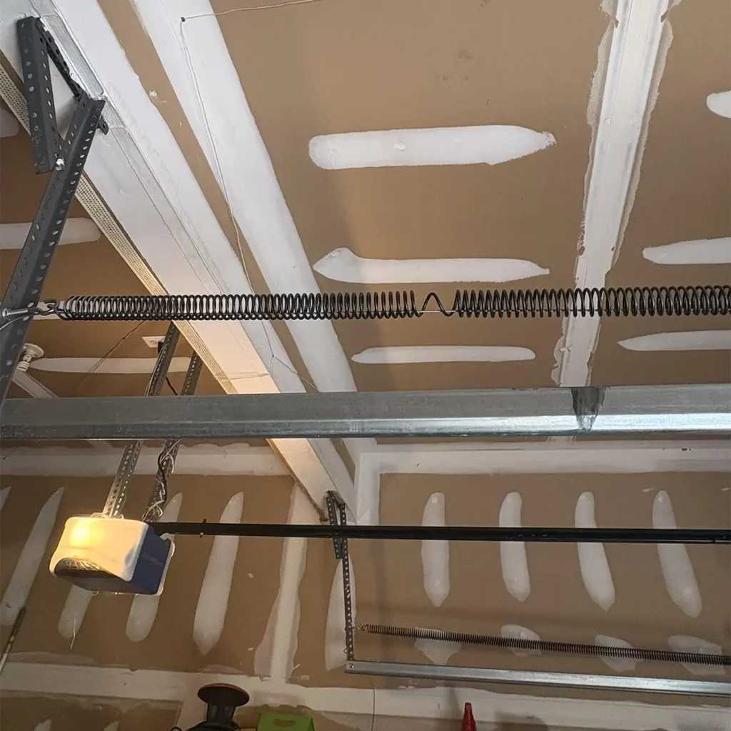 Damaged garage door spring needing replacement showing a snapped torsion spring with a visible gap