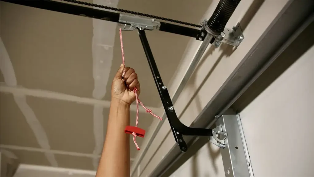 Garage door emergency release cord hanging from the opener mechanism, showing the red handle and cord for manual door operation during power outages