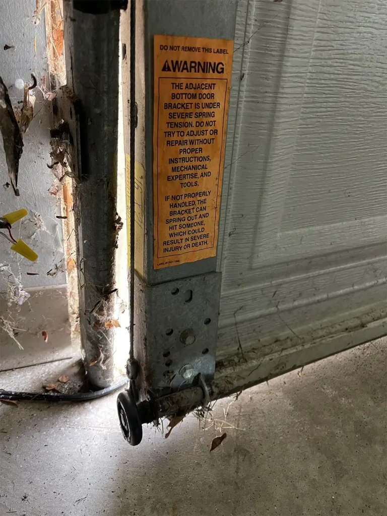 Garage door misaligned off tracks showing a roller that has come out of the guide rail with the door hanging at an angle