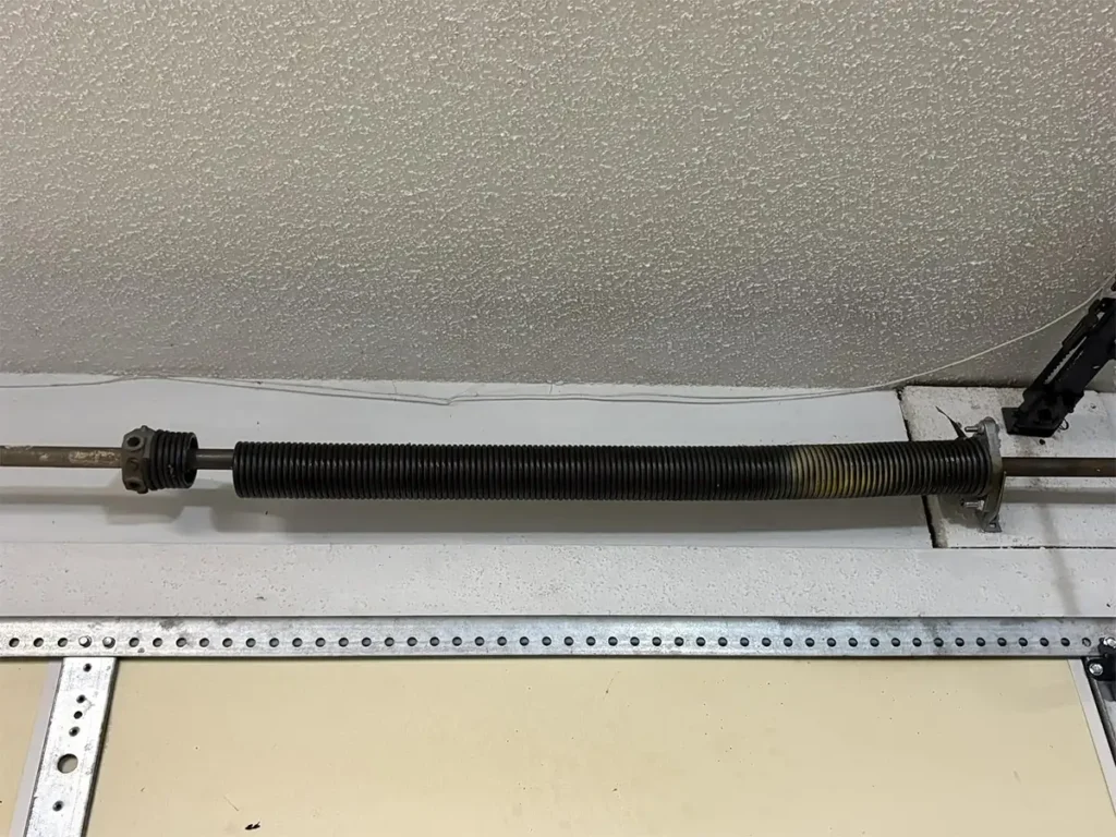 Garage door spring snapped clean in half, showing a visible break with the two pieces separated on a residential garage door system