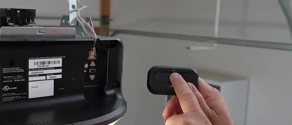 Pairing a garage door remote to the automation motor, showing the "Learn" button on the motor housing being pressed to program a new remote