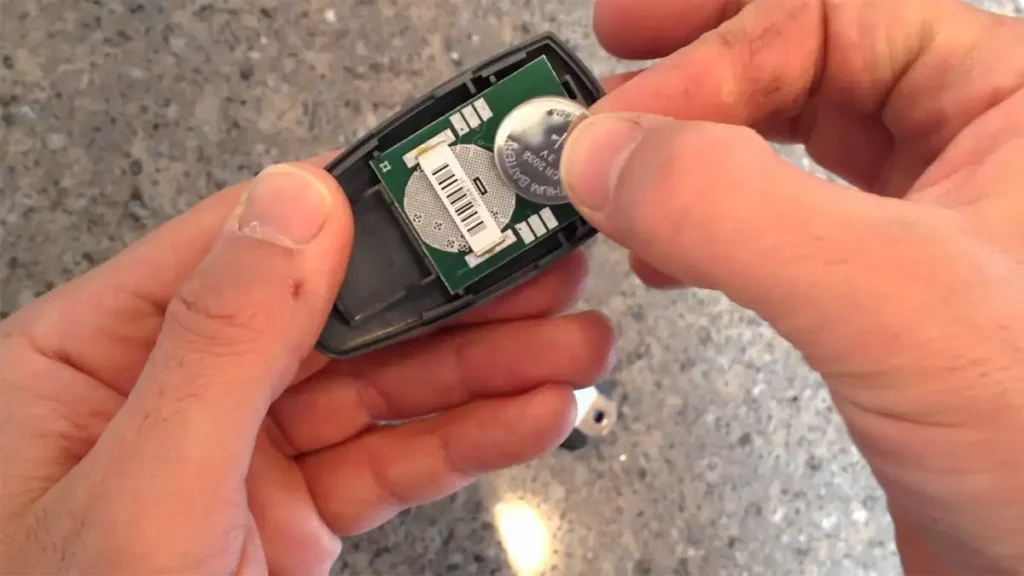 Replacing a garage door remote battery, showing the remote casing open with the old battery being removed and a new battery ready for installation