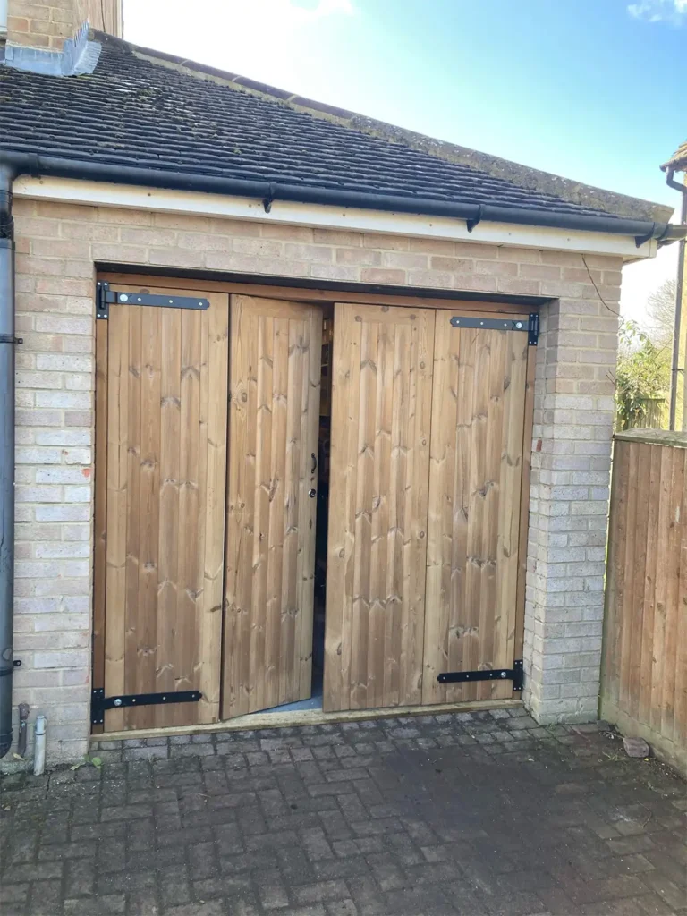 Side-hinged bi-fold timber garage door on a residential property with a natural wood finish and bifold opening mechanism